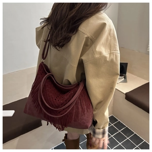 Detail of burgundy suede tote bag featuring long fringes and bohemian woven patterns