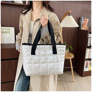 Detail of silver quilted tote bag with wide black straps in a cozy home setting
