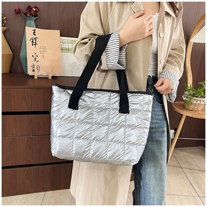 Detailed close-up of a silver quilted down tote bag with black woven handles and sleek finish