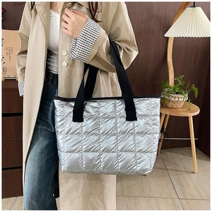 Detail of silver quilted tote bag with wide black handles shown as crossbody wear