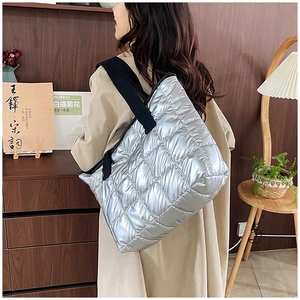 Silver quilted oversized tote bag with black straps worn over a classic khaki trench coat