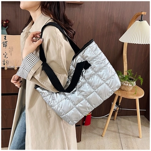 Detail of silver quilted tote bag with black wide straps shown in a lifestyle setting