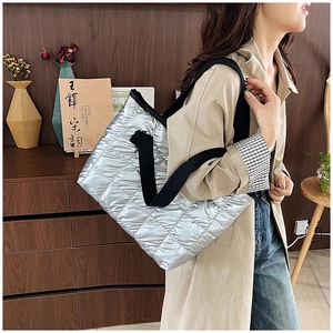 Detail of silver quilted tote bag with metallic finish and wide black shoulder strap