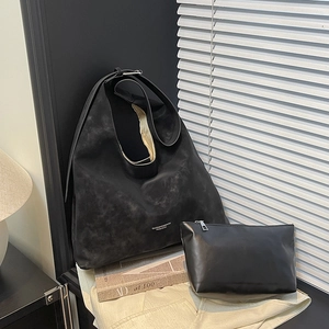 Grand sac cabas noir en suède avec pochette présenté contre un mur au style minimaliste