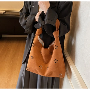 Détail du sac seau en daim marron avec motifs floraux découpés au laser et poignée nouée