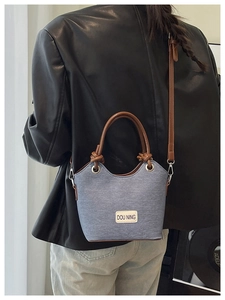 Détail du sac seau en denim avec écusson logo en cuir et ferrures métalliques argentées