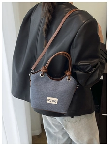 Détail du sac seau gris et marron avec patch logo Dou Ning porté sur une veste en cuir noir
