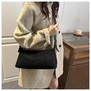 Detail of minimalist black suede shoulder bag with visible stitching and adjustable strap
