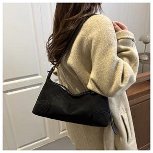 Close-up of vintage underarm bag in black suede texture worn by a model in a modern home