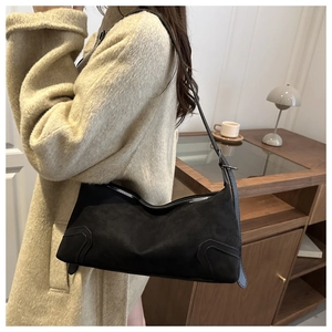 Detail of black matte suede shoulder bag worn with a beige tweed coat in warm indoor light