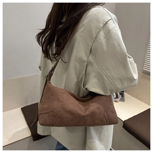 Detail of brown suede baguette bag featuring curved stitching and adjustable shoulder strap