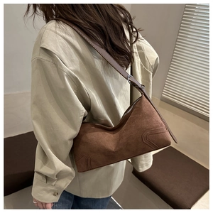 Detail of dark brown suede crescent shoulder bag with silver hardware on a female model