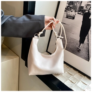 Detail view of cream white leather bucket bag featuring a knotted strap and metal rings