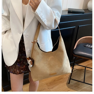 Détail du sac cabas en daim kaki avec breloque chien porté par un mannequin en décor épuré