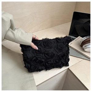 Detail of elegant black clutch bag featuring 3D chiffon rose flowers and zip closure