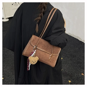 Brown suede underarm bag with cute bear charm and striped scarf shown on a shoulder