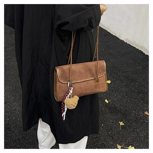 Detailed shot of brown suede shoulder bag with bear pendant on model wearing a black coat