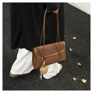 Close-up of brown suede shoulder bag with cute bear charm and plaid scarf detail
