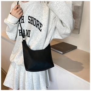 Minimalist black matte leather hobo bag with slim strap shown on model's shoulder