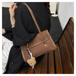 Detail of brown matte underarm bag featuring a cute bear charm and woven ribbon strap