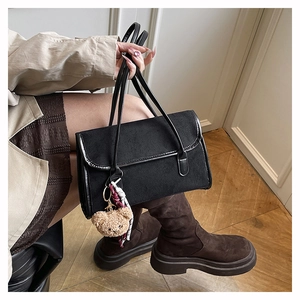 Detail of minimalist black suede shoulder bag featuring a cute brown teddy bear charm accessory
