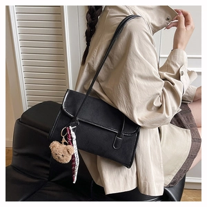 Detail of black matte shoulder bag with cute bear charm and woven rope accessory