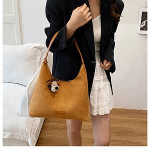 Grand sac cabas en daim marron avec charm chien, porté dans un studio minimaliste