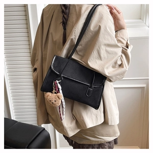 Detailed side view of black shoulder bag with teddy bear charm and ribbon accent