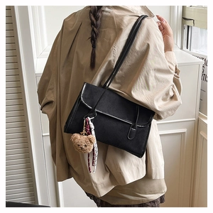 Detail of black suede shoulder bag with cute brown bear charm and braided rope accessory