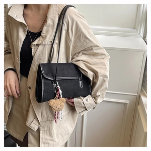 Detail of black suede shoulder bag with cute brown bear charm on beige trench coat