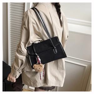 Detail of black canvas shoulder bag with plush bear charm and plaid scarf accent