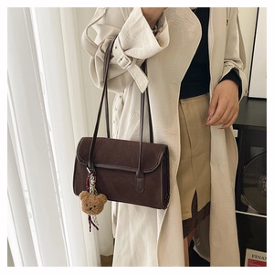 Detail of dark brown suede shoulder bag featuring a cute plush bear pendant accessory