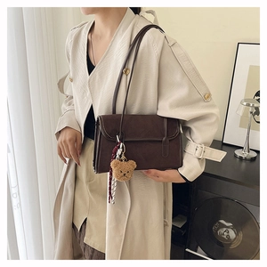Detail showing matte dark brown suede shoulder bag with plush bear and silk scarf decor