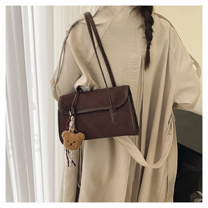 Detail of dark brown matte shoulder bag with cute bear charm worn over a beige coat