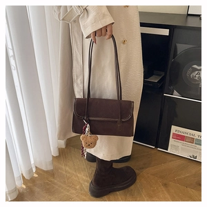 Detail of dark coffee suede shoulder bag with plush bear charm and plaid scarf accessory