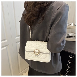 Detailed macro shot of white quilted flap bag with pearl gold buckle and chain strap