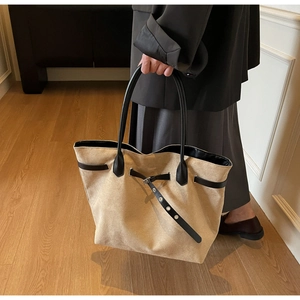 Close-up of beige tote bag with black leather straps and silver metal eyelet details