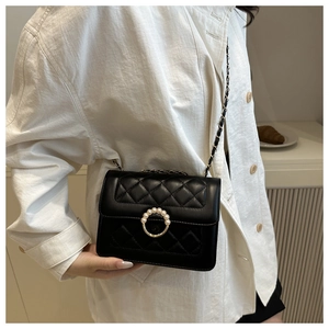 Side view of black quilted crossbody bag with pearl buckle on a white shirt
