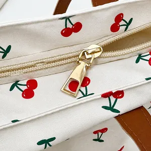 Detail eines glatten Goldreißverschlusses an weißer Canvas-Tasche mit Kirschmuster