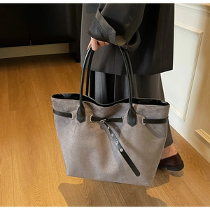 Detail of grey suede tote bag with metal eyelets and black leather handles in daily use
