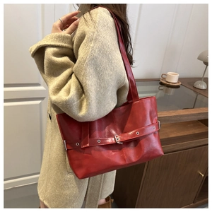 Detail of red faux leather tote bag with buckle strap on a beige coat model