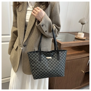 Detail of grey patterned tote bag with golden logo plate on a brown blazer outfit