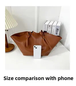 Brown leather tote bag side view showing capacity next to a smartphone
