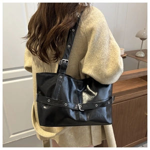 Close-up of black glossy leather tote bag with silver belt buckle and adjustable strap