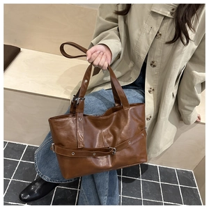 Caramel brown tote bag with decorative buckle straps shown on a warm-toned wooden table