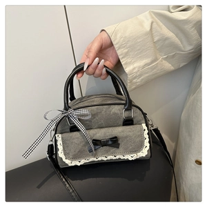 Detail of grey denim boston bag with lace trim, black bow, and plaid ribbon handle