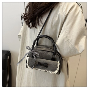 Detail of grey denim pillow bag featuring white lace trim and black bow ribbons