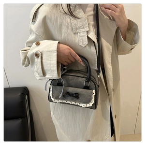 Detail of dark gray bowling bag with lace trim and black bow decoration shown on a model