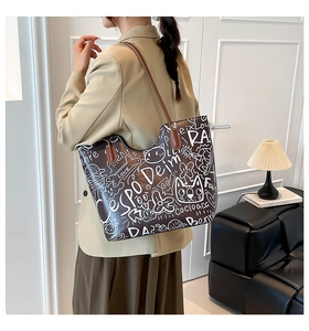 Close-up of a large tote bag featuring artistic white graffiti and brown leather straps