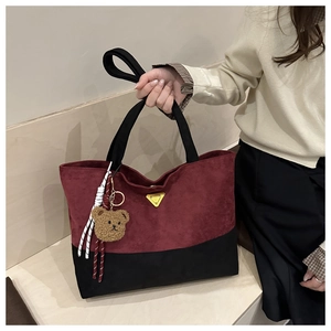 Detail of color-block bucket bag with burgundy suede and metallic triangle emblem